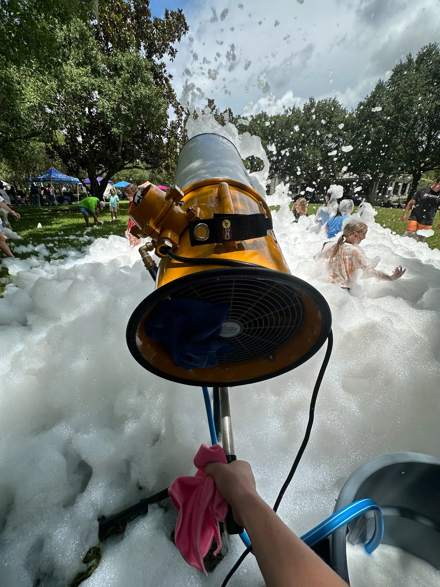 Attendant aiming a professional foam cannon over a foam-covered lawn