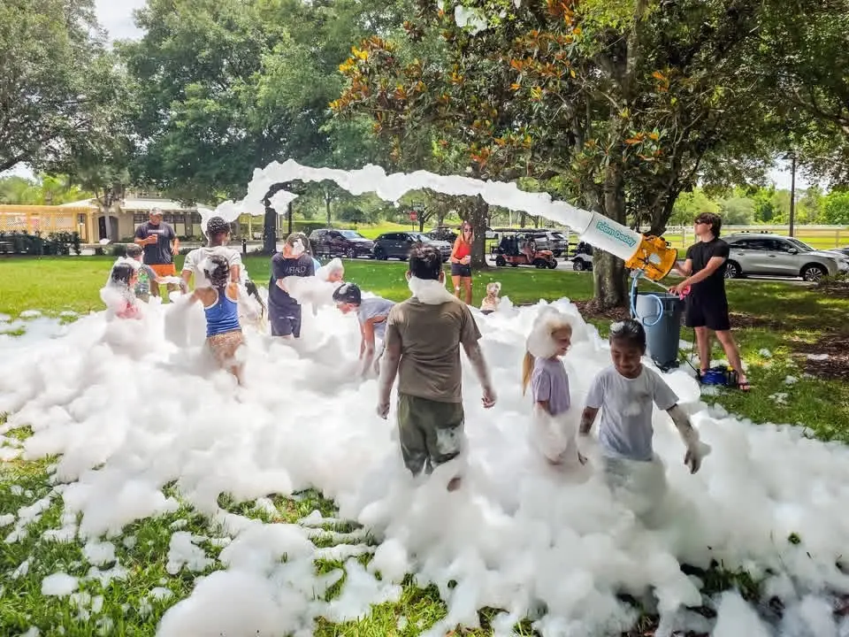 Foam cannon arcing foam over a park lawn full of guests at a foam party